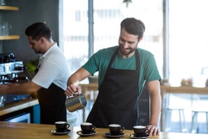 Smiling waiter making cup of coffee at counter in cafe
