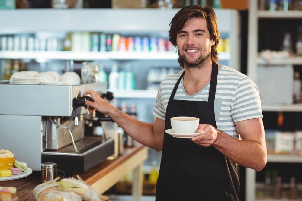 Portrait of smiling waiter holding cup of coffee in cafe